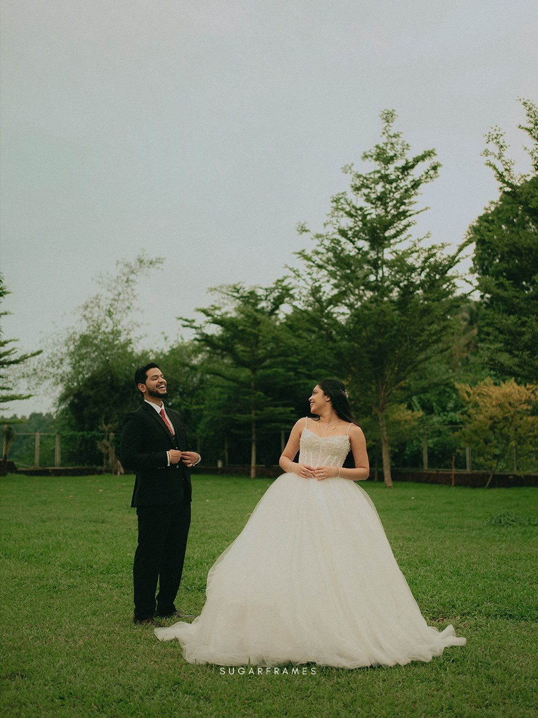 A newlywed couple laughing together in a green garden