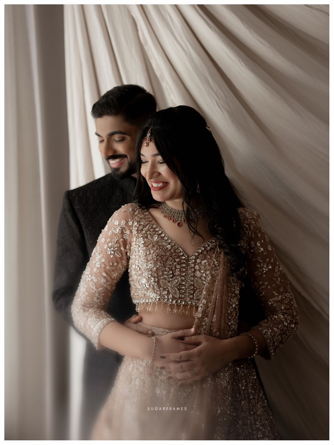 An engaged couple smiling together beside softly draped fabric